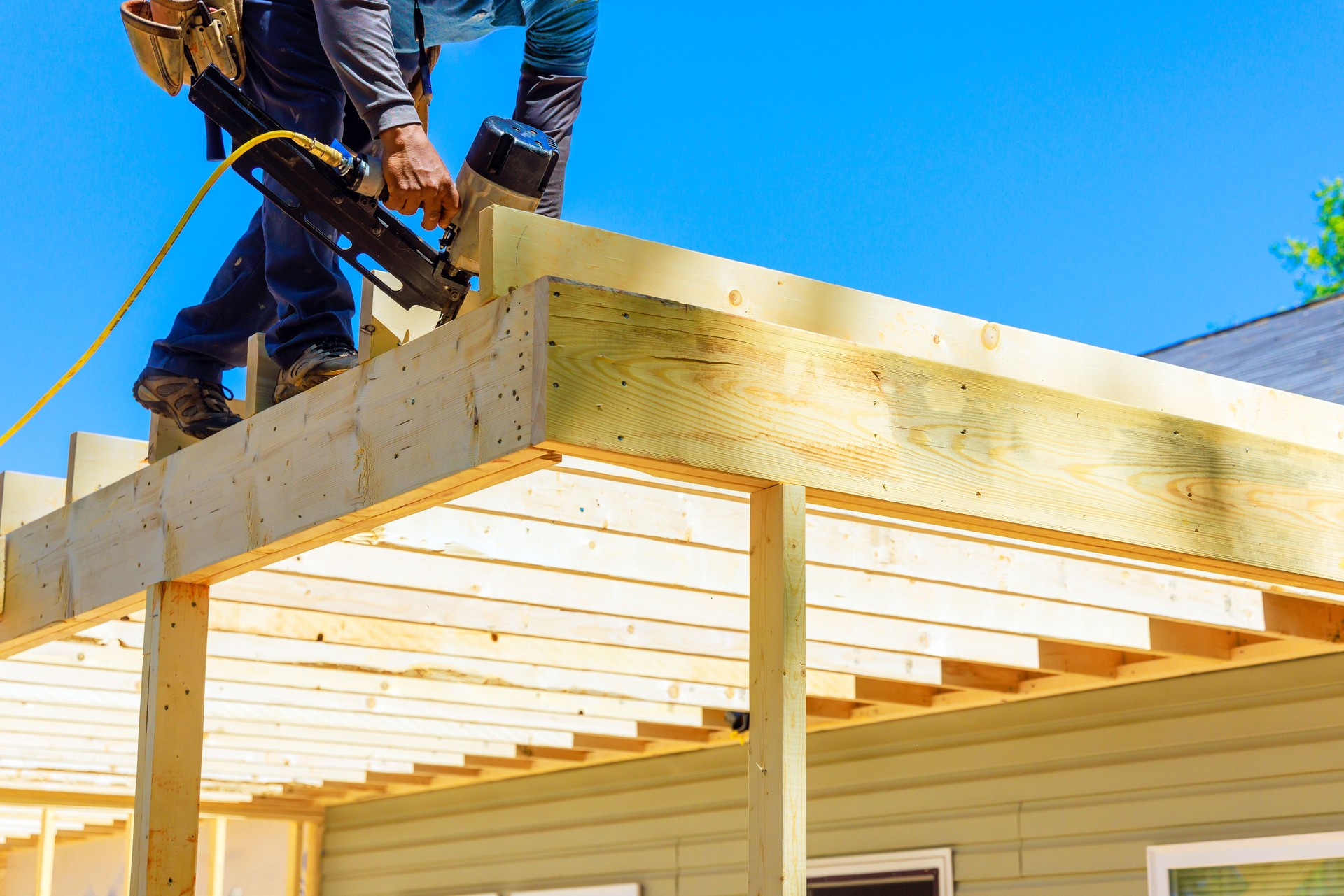 Worker installing beams with an air nail hammer a nailing wooden planks