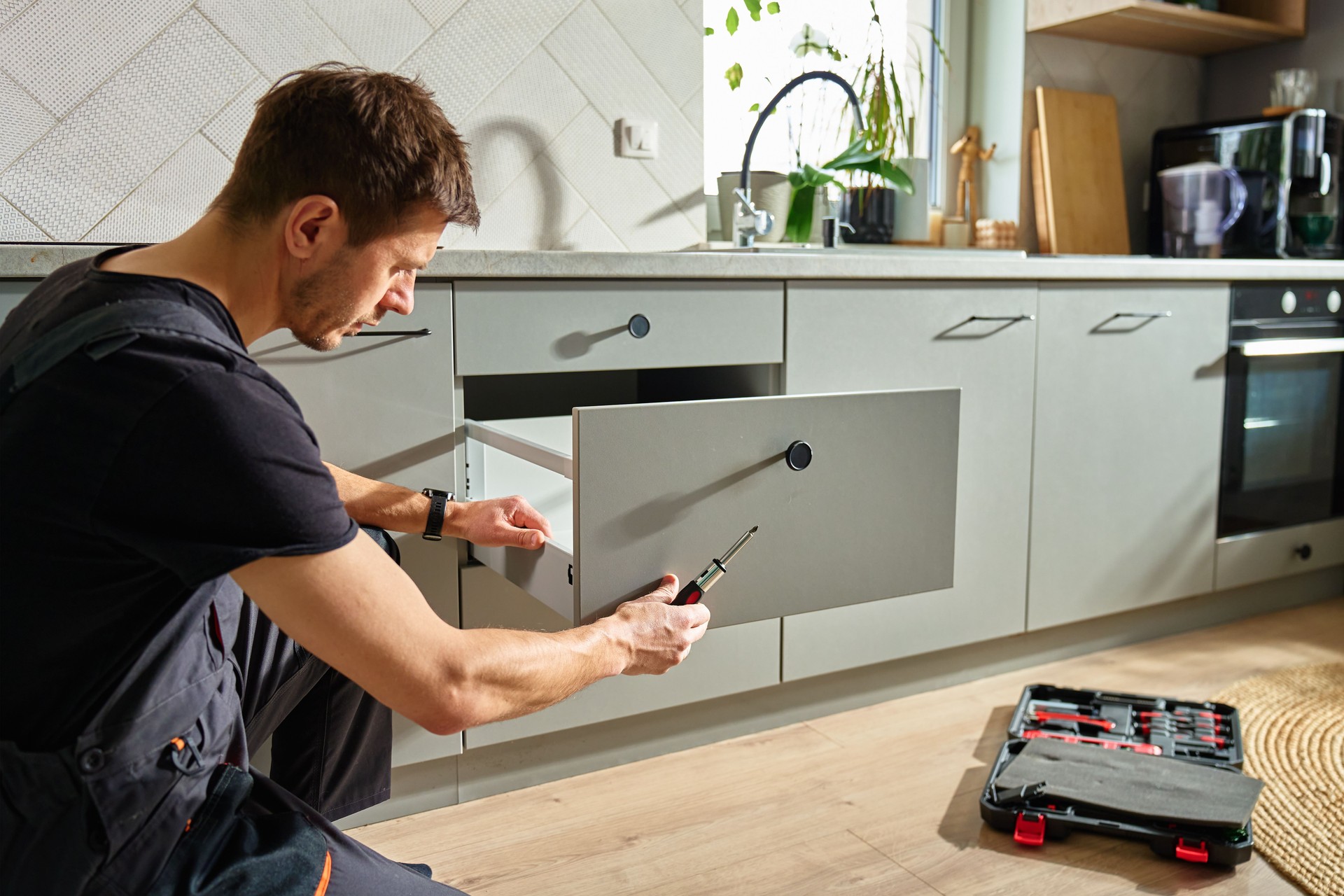 Carpenter installing and adjusting drawer front in modern kitchen cabinet